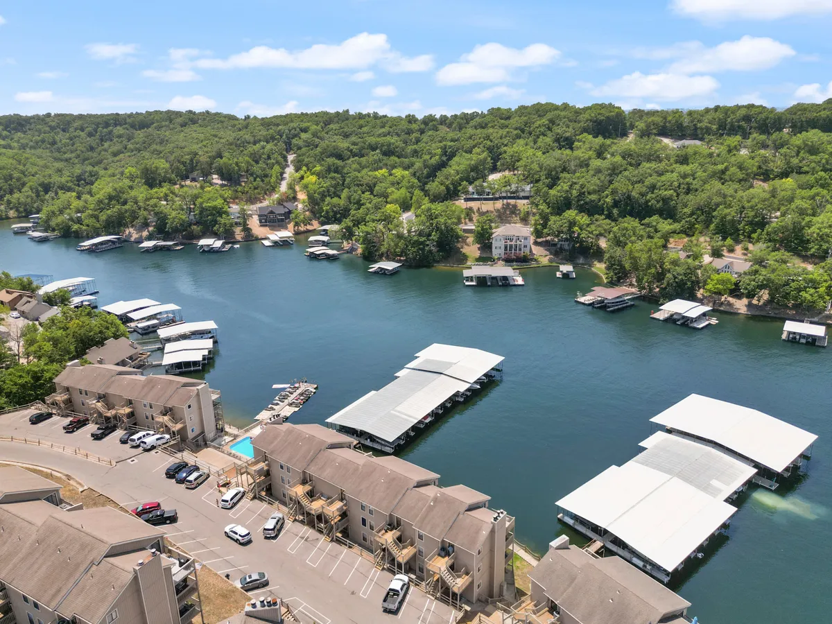A wide exterior shot capturing the waterfront area with visible marinas, lush surrounding greenery, and residential buildings along the shoreline. Boats are docked nearby, and the setting exudes a relaxed vibe, perfect for boating, fishing, or simply enjoying the scenic lake environment.
