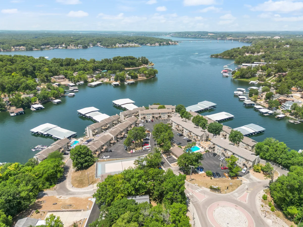 A sweeping view captures the lake, surrounding poolside buildings, well-maintained docks with boats, and expansive green spaces. The scene radiates tranquility and invites thoughts of boating, swimming, and family picnics by the water.