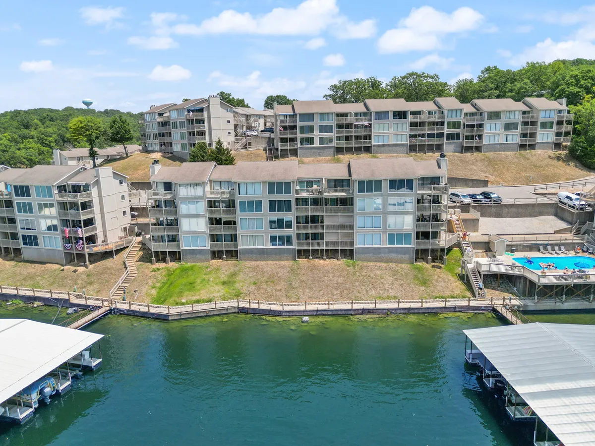 A vibrant waterfront scene featuring a spacious pool area set against a backdrop of greenery and a boat dock along the lake’s edge. The setting balances the appeal of both swimming and easy access to lake activities like boating and fishing.