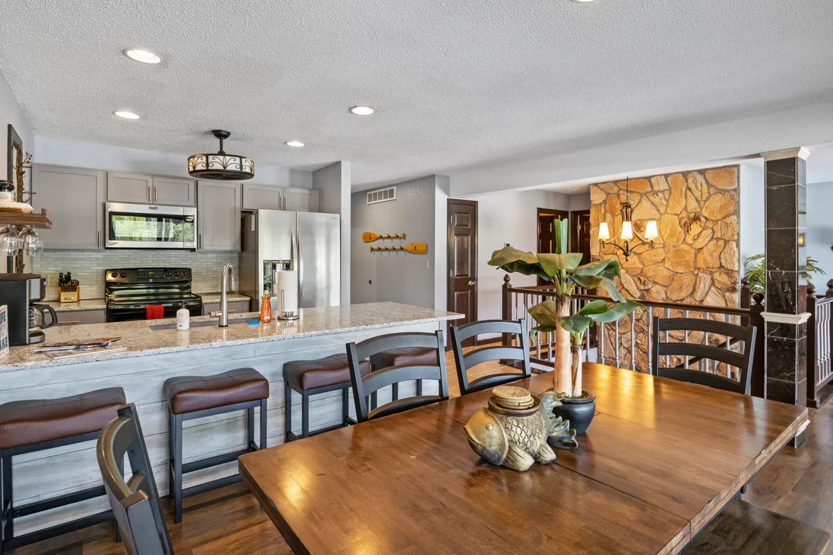 A spacious, modern clubhouse kitchen with a large island, dining table, stone accent wall, and kitchen appliances. The setting feels inviting and ready for gatherings or snack preparation after a day at the pool.