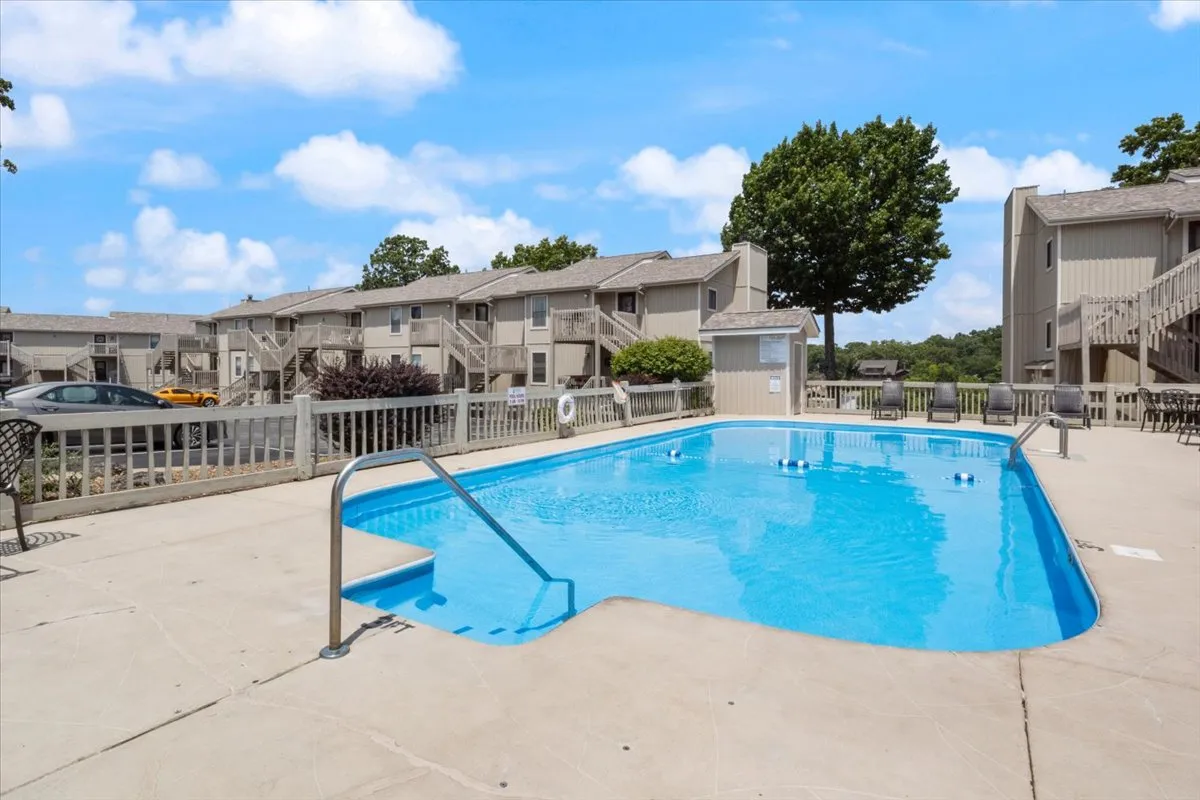 A vibrant swimming pool area surrounded by landscaped trees and neighboring buildings, inviting guests to swim, lounge, or gather for social events. The bright atmosphere signals fun, relaxation, and community.
