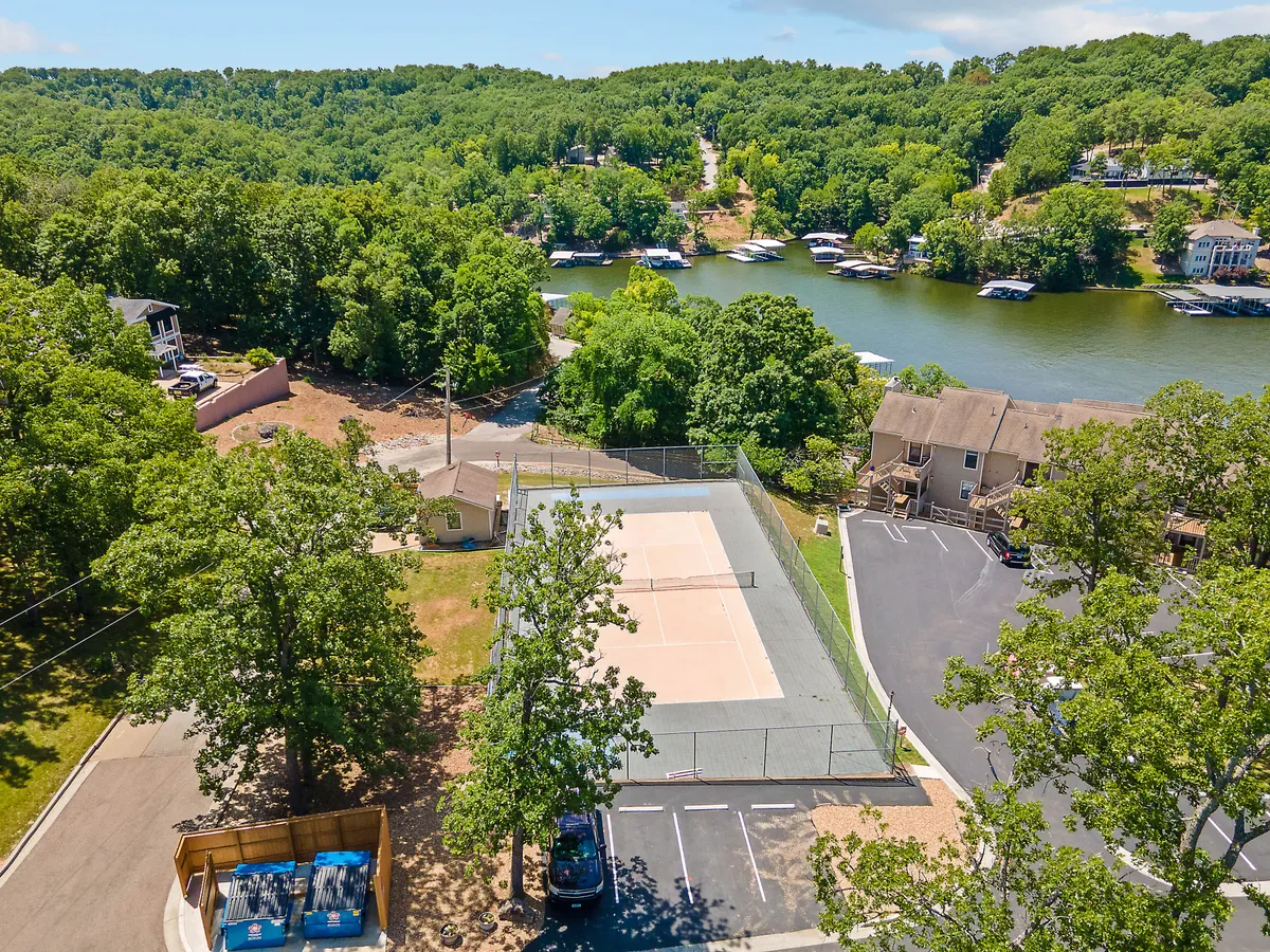 This image features a well-maintained basketball court overlooking the lake, surrounded by trees and adjacent to a parking area. The setting is active yet serene, illustrating opportunities for sports and outdoor recreation within the community.