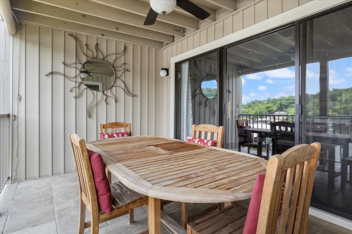 This image shows an inviting outdoor dining area featuring a wooden table, sun mirror, sliding glass doors, and comfortable outdoor chairs. The view through the glass doors hints at a seamless transition between the secure interior of the property and its welcoming outdoor space.