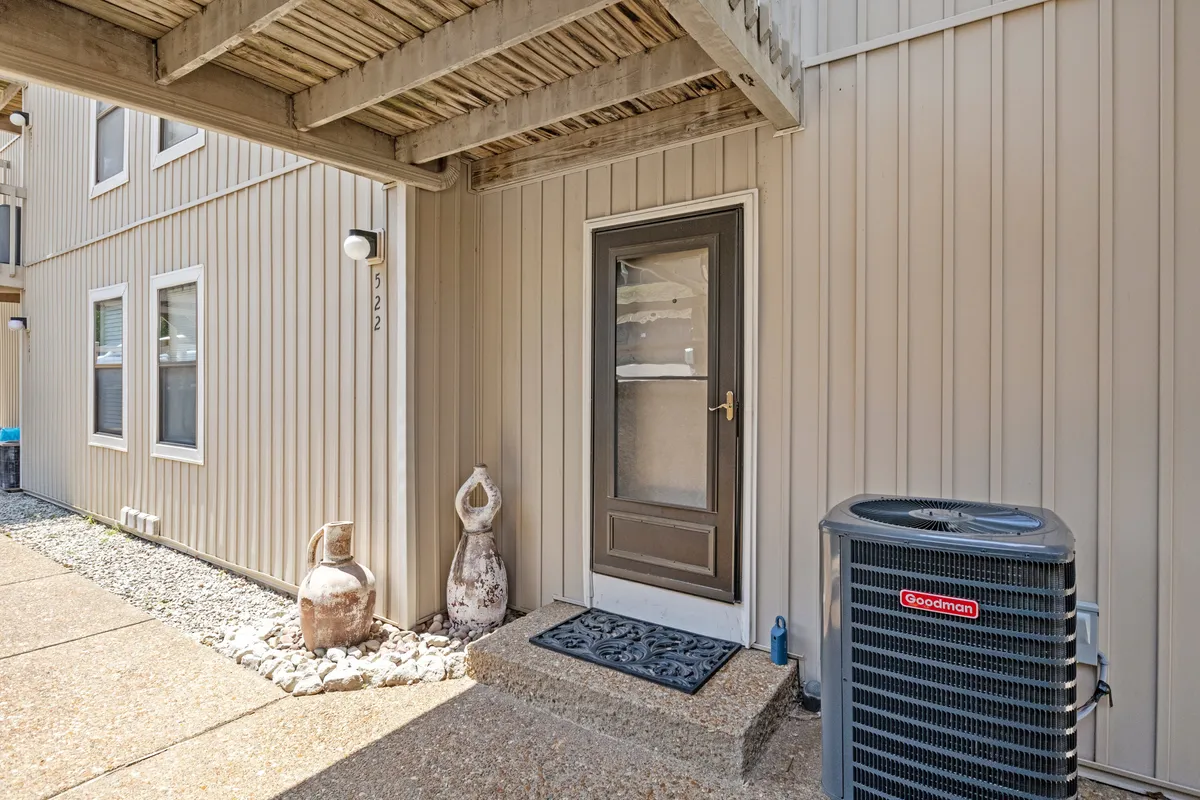 A clear view of the front door, accented by decorative sculptures and an air conditioning unit. The scene sets a welcoming tone and subtly suggests modern entry features, such as smart locks or video doorbells.